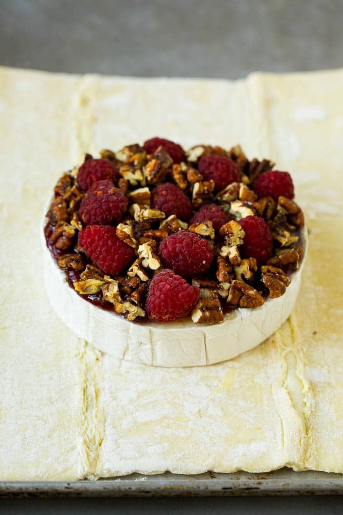 Baked Brie Recipe | Pastry Wrapped Brie #brie #cheese #appetizer #pecans #raspberries #fuyos A wheel of cheese topped with jam, raspberries and pecans.