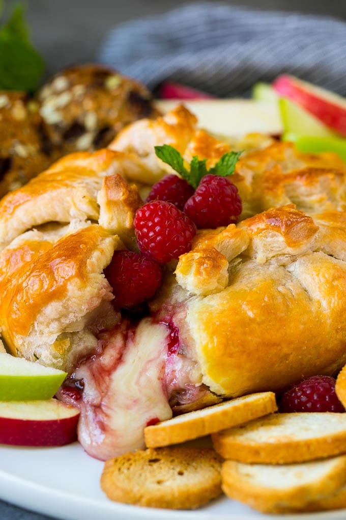 Baked Brie Recipe | Pastry Wrapped Brie #brie #cheese #appetizer #pecans #raspberries #fuyos Baked brie cut open with cheese spilling out.
