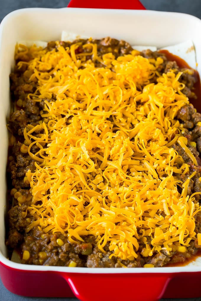 Mexican Lasagna Recipe | Mexican Casserole #mexican #lasagna #groundbeef #beans #dinner #cheese #fuyos Layers of tortillas, ground beef and shredded cheese in a baking dish.