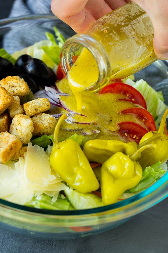 Olive Garden Salad Recipe | Italian Salad #salad #lettuce #olives #sidedish #dinner #fuyos Dressing being poured over a bowl of salad.