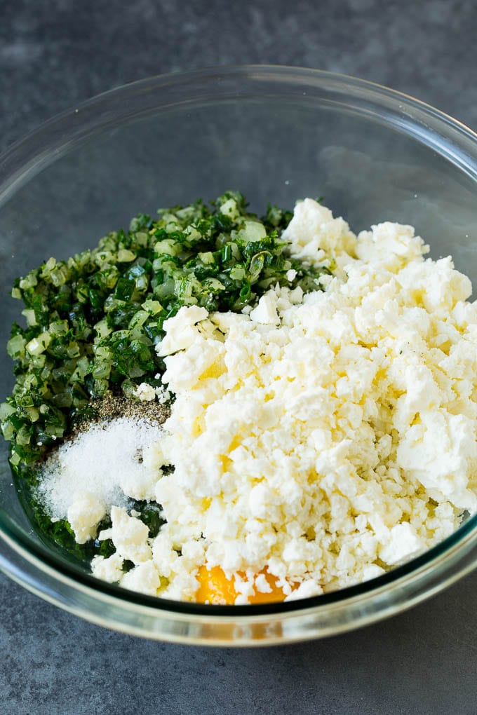 Spanakopita Recipe #appetizer #snack #spinach #cheese #fuyos Spinach, onions, herbs and feta cheese in a bowl.