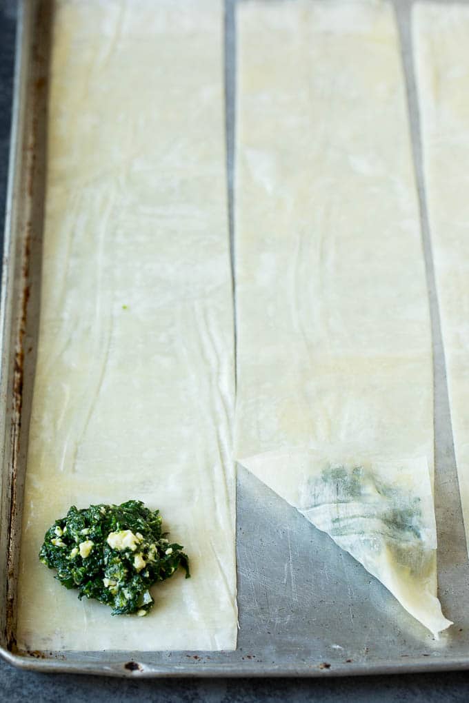 Spanakopita Recipe #appetizer #snack #spinach #cheese #fuyos Strips of phyllo dough with spoonfuls of filling on top.
