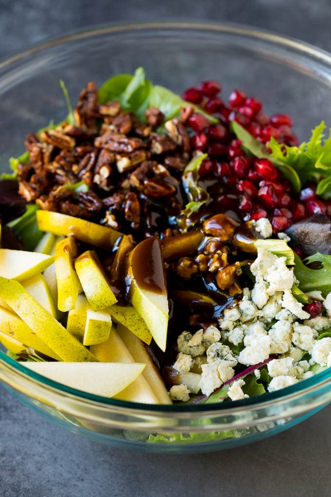 Pear Salad Recipe #salad #pears #fall #winter #dinner #fuyos Balsamic dressing poured over a bowl of mixed greens, fruit and pomegranate seeds.