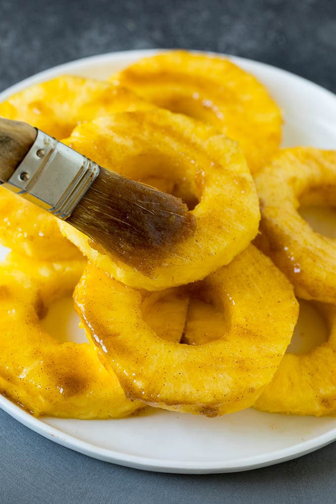 A brush coating fruit slices with butter and brown sugar.