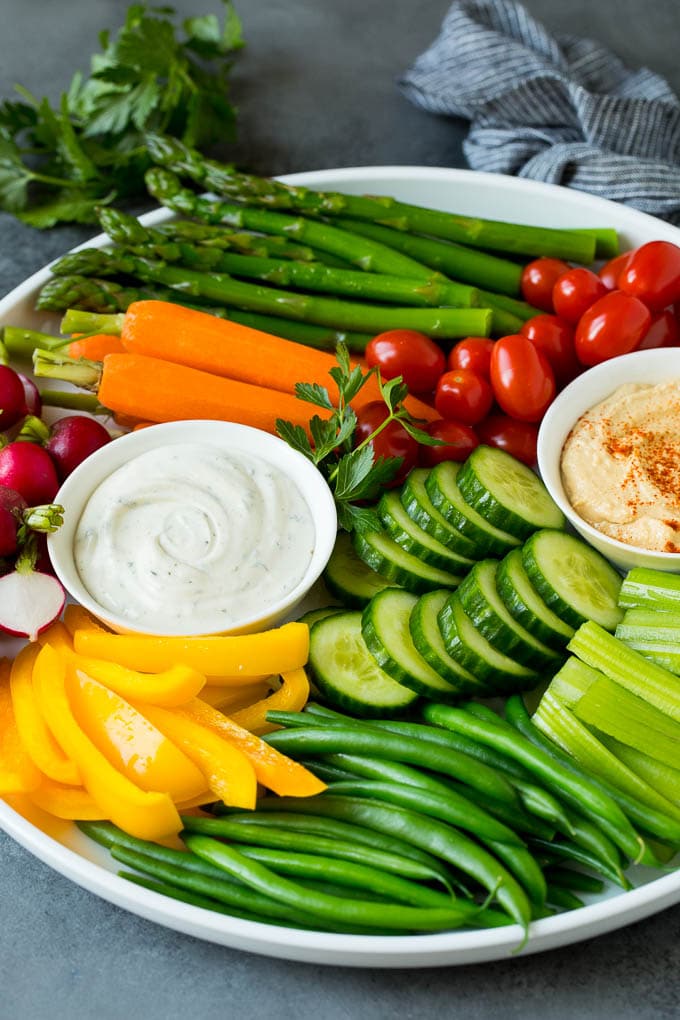 A veggie tray filled with fresh vegetables and two types of dip.