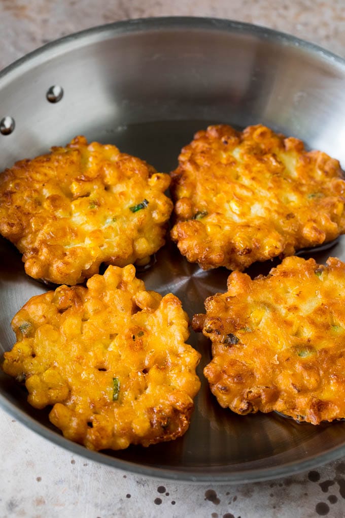 These crispy corn fritters are easy to make and are the perfect appetizer or lighter main course. #corn #fuyos Corn cakes in a pan of oil.