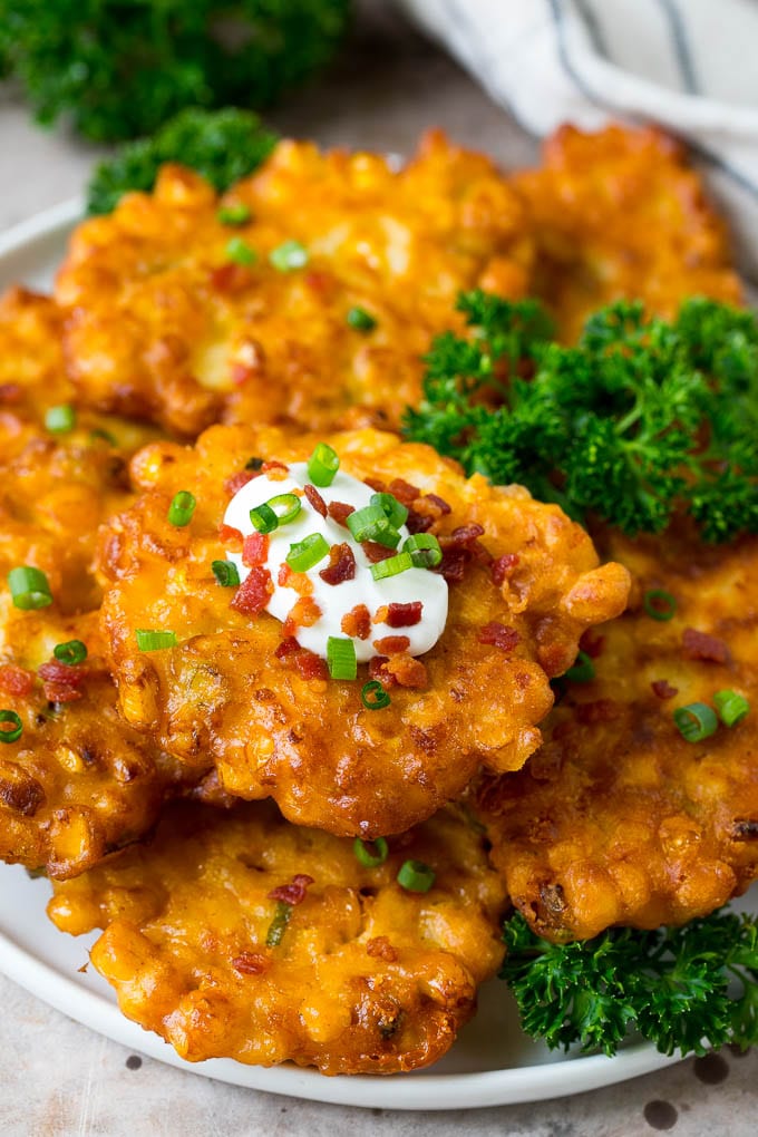 These crispy corn fritters are easy to make and are the perfect appetizer or lighter main course. #corn #fuyos A plate of corn fritters garnished with parsley, and topped with sour cream.