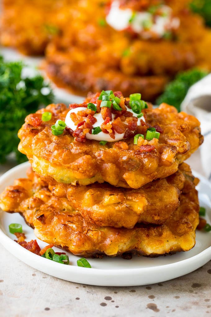 These crispy corn fritters are easy to make and are the perfect appetizer or lighter main course. #corn #fuyos A stack of corn fritters topped with bacon, sour cream and green onions.