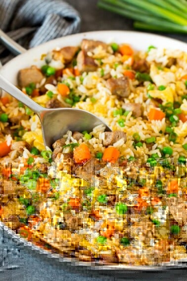 A pan of pork fried rice with a serving spoon in it.