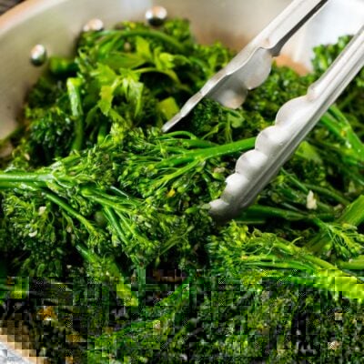 Tongs serving up a portion of sauteed broccolini.