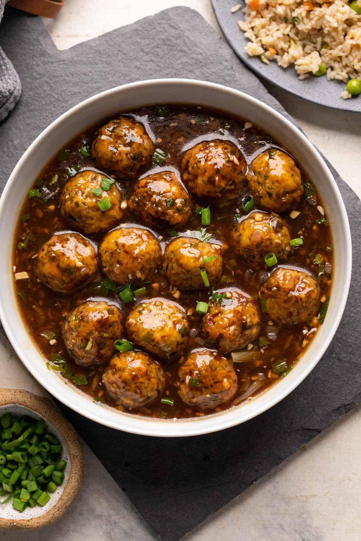 Manchurian Vegetariano | Come preparare il Manchurian 2 Manchurian Vegetariano servito in una ciotola bianca con riso fritto e cipollina verde a lato