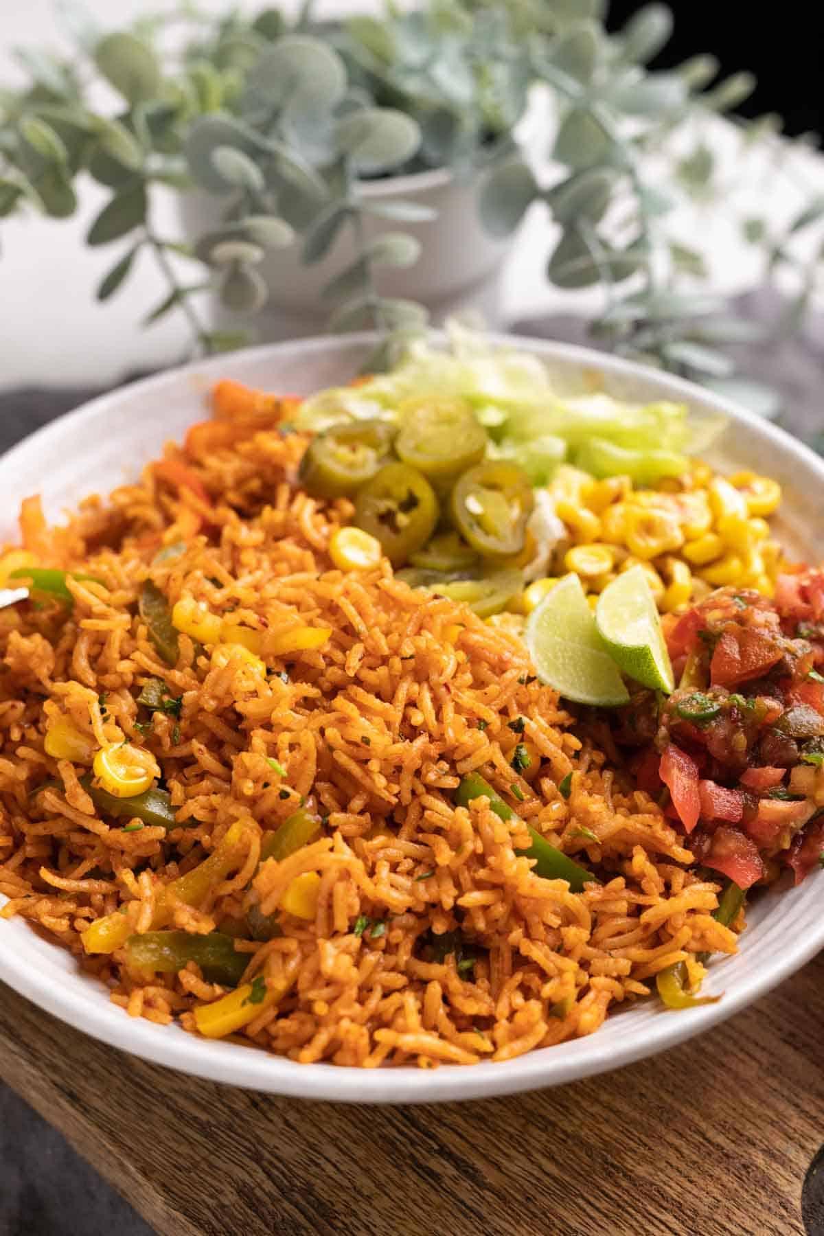Riso Messicano in Pentola a Pressione (Arroz Rojo) 2 Riso Messicano Instant Pot servito in una ciotola con lattuga, mais, salsa, jalapeños e spicchi di lime sul lato.