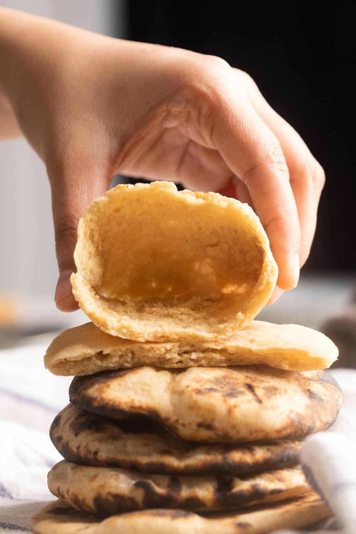 Ricetta del Pane Pita Integrale 2 Immagine di una mano che tiene un pane pita integrale appena sfornato, aperto per mostrare la tasca interna, soffice e invitante.