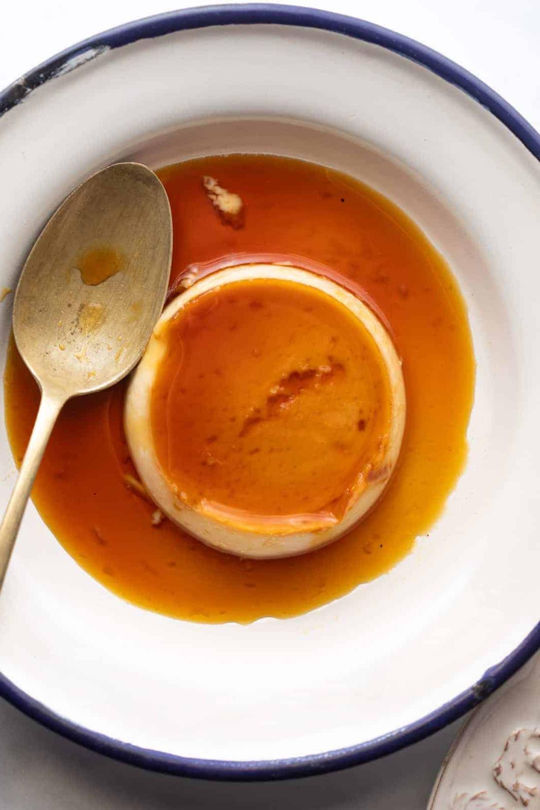 **Budino al Cocco e Caramello sul Fornello** 2 Primo piano di budino al caramello e cocco servito su un piatto bianco con bordo blu e un cucchiaio