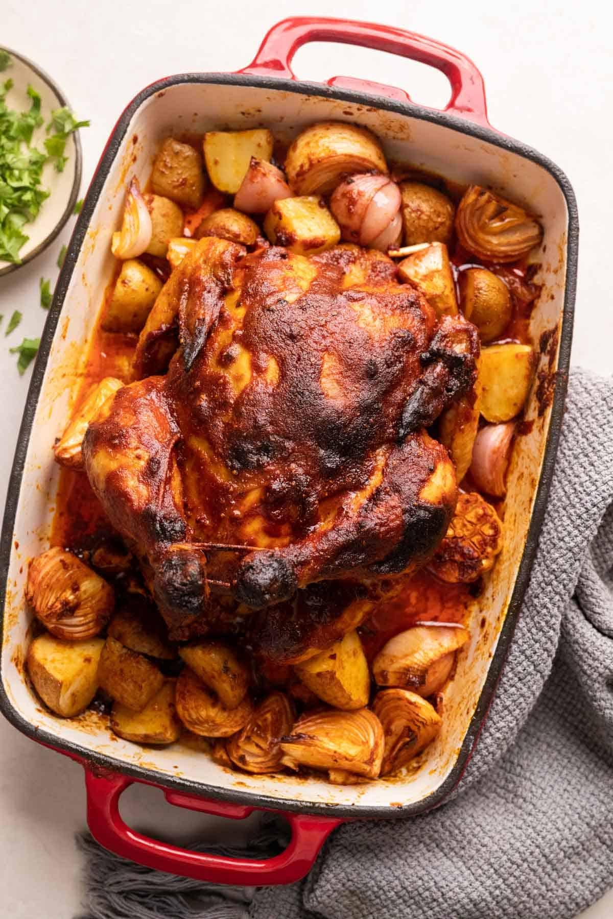 Pollo Arrosto Intero al Masala all'Indiana 2 Pollo arrosto indiano servito su un letto di cipolle, patate e aglio in una teglia rossa