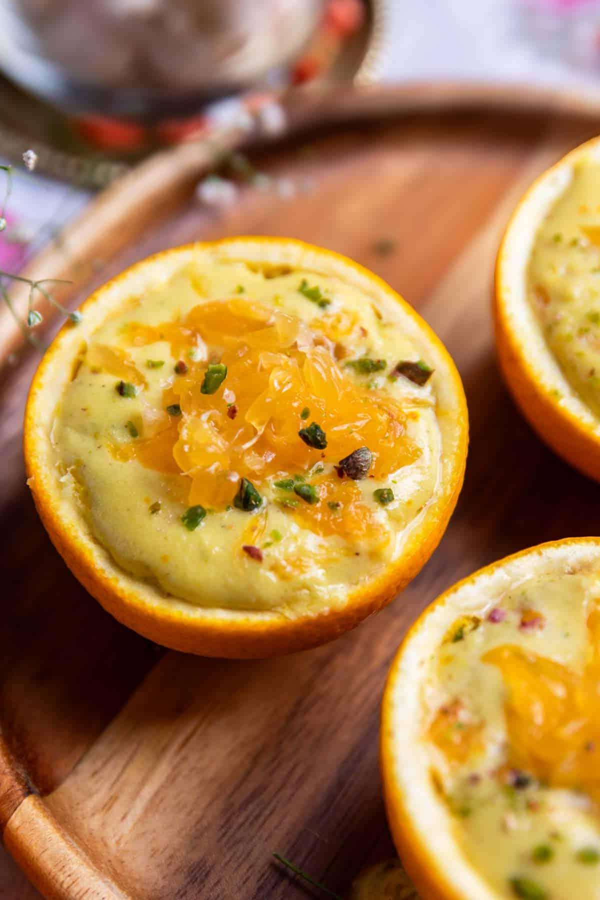 Budino di Makhana all'arancia 3 Primo piano di budino di makhana all'arancia servito in coppette ricavate da scorze d'arancia con pistacchi tritati