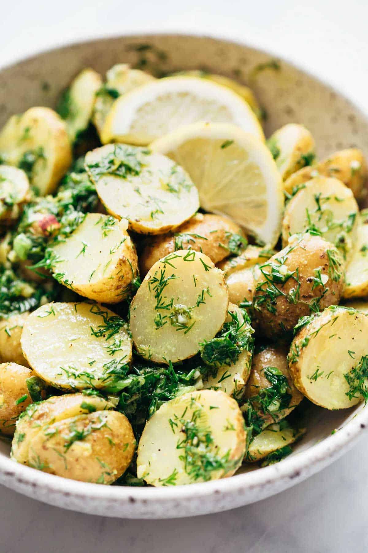Insalata di Patate Salutare al Limone e Aneto (Senza Maionese) 3 Primo piano dell'Insalata di Patate Leggera al Limone e Aneto (senza maionese) servita in una ciotola bianca maculata con spicchi di limone