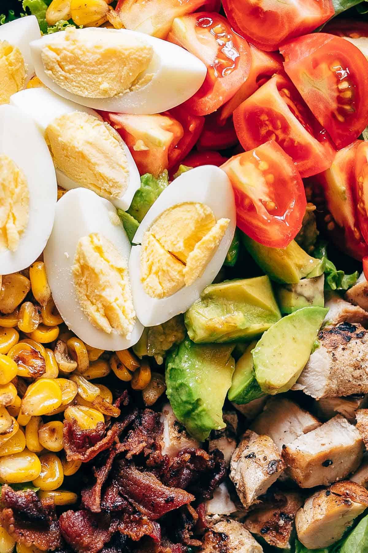 Un'altra prospettiva invitante dell'Insalata Cobb di Pollo, pronta per essere gustata. Tutti gli ingredienti freschi e ben visibili, pronti per offrire un pasto sano, nutriente e delizioso. Perfetta per ogni occasione e facile da assemblare. #insalata #pollo #ricettasana #cena #ingredientifreschi Una splendida Insalata Cobb di Pollo presentata in una ciotola, con strati ben distinti di lattuga, pomodori, pollo, pancetta, mais e uova sode. Un pasto equilibrato e visivamente appetitoso.