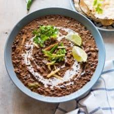 Facile Dal Makhani in Slow Cooker 4 Dal Makhani guarnito con panna, coriandolo, zenzero, lime e servito in una ciotola blu.