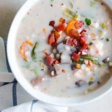 Zuppa Cremosa di Pollo e Orzo a Cottura Lenta 4 Zuppa Cremosa di Pollo e Orzo in Slow Cooker guarnita con pancetta fritta e servita in una ciotola bianca.