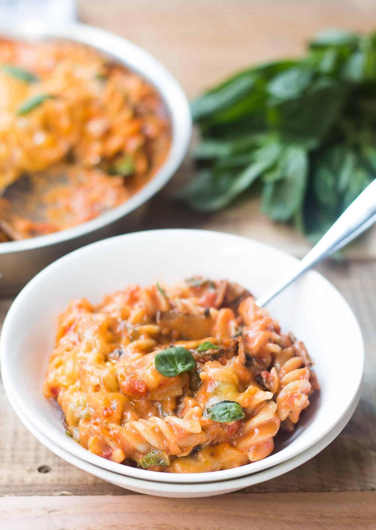 Pasta Domenicale di Verdure Tutto Incluso 4 Una confortante ciotola di pasta vegetariana della domenica con formaggio, guarnita con basilico fresco e servita in una ciotola bianca.