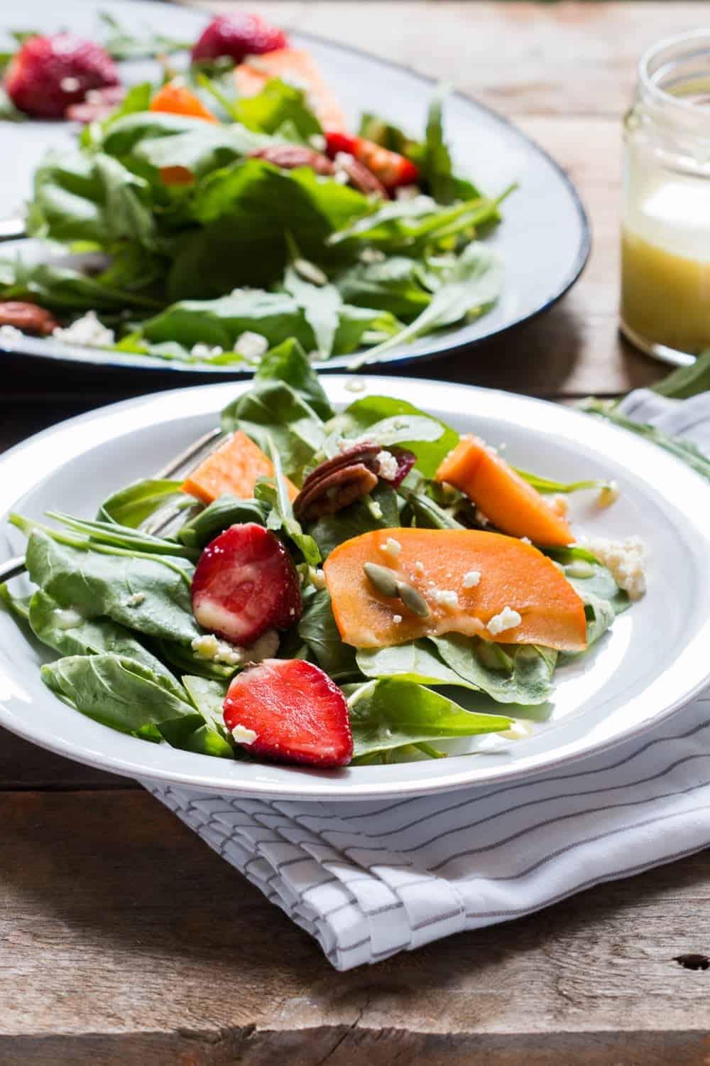 Insalata Colorata con Ricotta e Frutta Insalata di Verdure, Cachi e Ricotta con Vinaigrette all'Arancia Amara servita in un piatto bianco