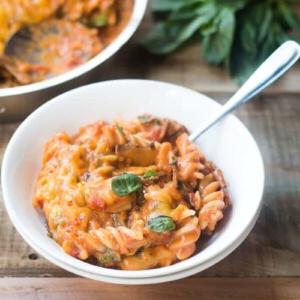 Pasta Domenicale di Verdure Tutto Incluso 5 Una confortante ciotola di pasta vegetariana della domenica con formaggio, guarnita con basilico fresco e servita in una ciotola bianca.
