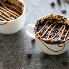 Torta in Tazza Senza Uova alla Banana, Cioccolato e Burro di Arachidi 6 Torta in tazza senza uova con banana, cioccolato e burro di arachidi in una tazza da tè, guarnita con burro di arachidi.