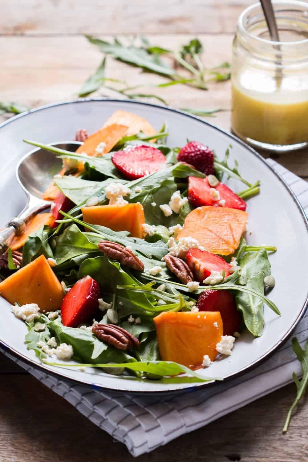 Insalata Fresca per Ogni Stagione Insalata di Verdure, Cachi e Ricotta con Vinaigrette all'Arancia Amara servita in un piatto bianco