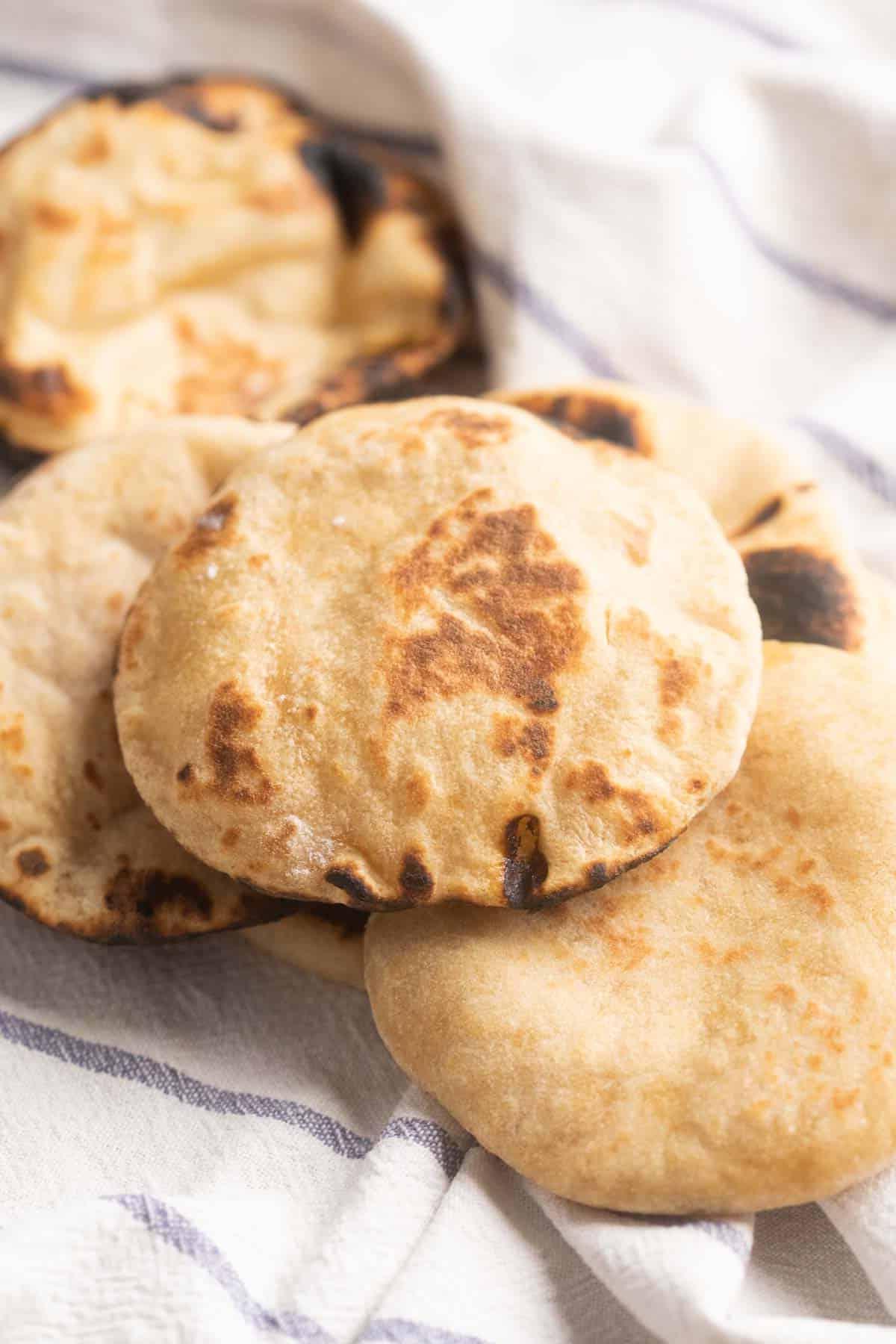 Ricetta del Pane Pita Integrale 7 Immagine di pani pita integrali appena sfornati, dorati e soffici, disposti su un panno da cucina a righe bianche, caldi e invitanti.