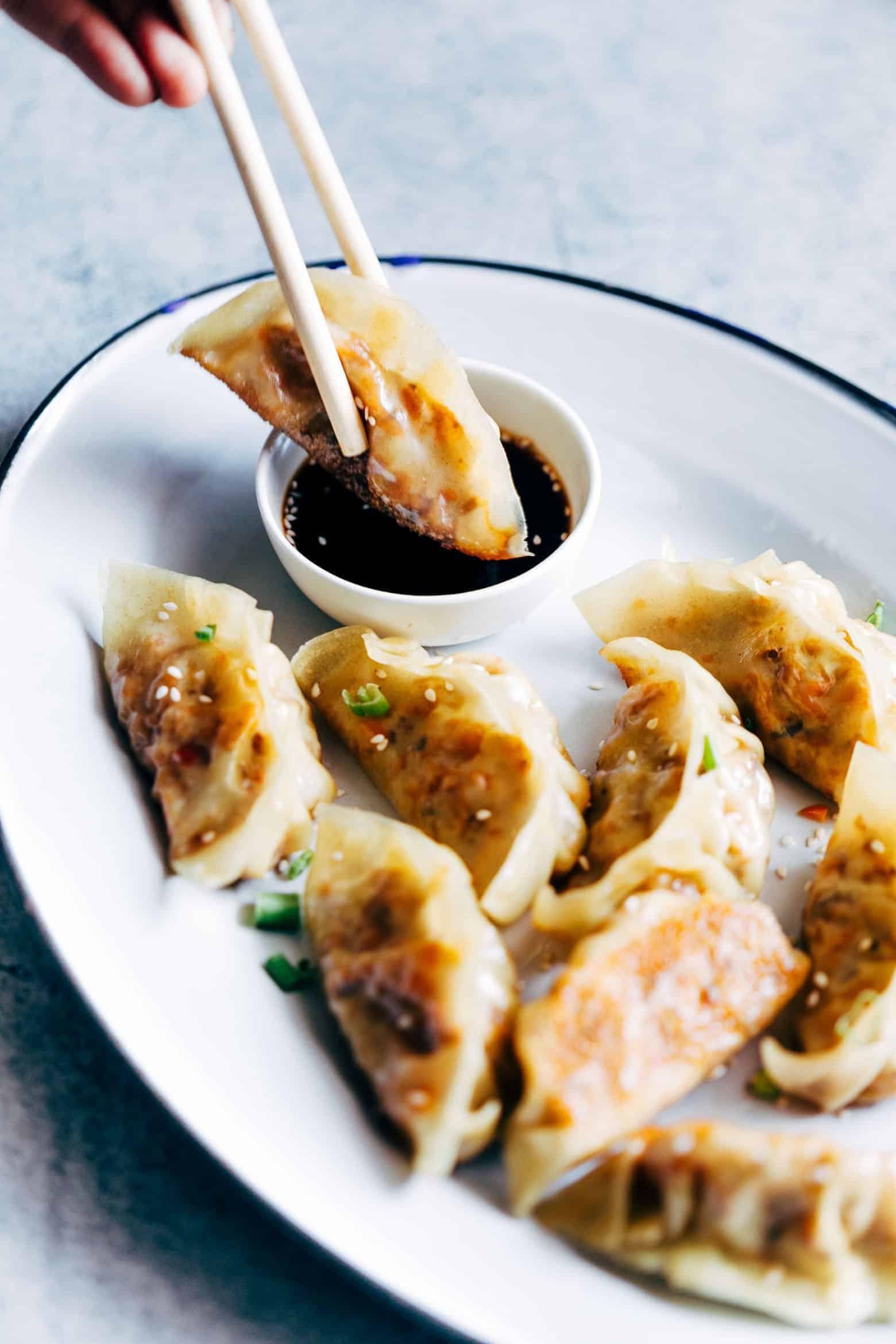 Gyoza Vegetariani con Carote e Paneer 7 Gyoza vegetariani dorati e croccanti, serviti con una ciotolina di salsa di accompagnamento, pronti per essere intinti e gustati.