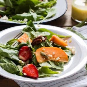 **Insalata di Verdure, Cachi e Ricotta con Salsa all'Arancia** 2 Insalata di Verdure, Cachi e Ricotta con Vinaigrette all'Arancia Amara guarnita con ricotta e servita in un piatto bianco.