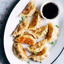Gyoza Vegetariani con Carote e Paneer 8 Gyoza vegetariani con carote e paneer serviti con una salsa di accompagnamento su un piatto bianco.