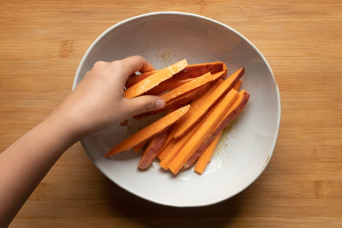 Patatine Dolci Croccantissime nella Friggitrice ad Aria 9 Immagine delle patate dolci fritte che vengono mescolate in una ciotola con i condimenti
