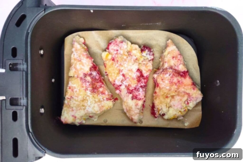 Raspberry scones arranged in a single layer in an air fryer basket, ready for cooking