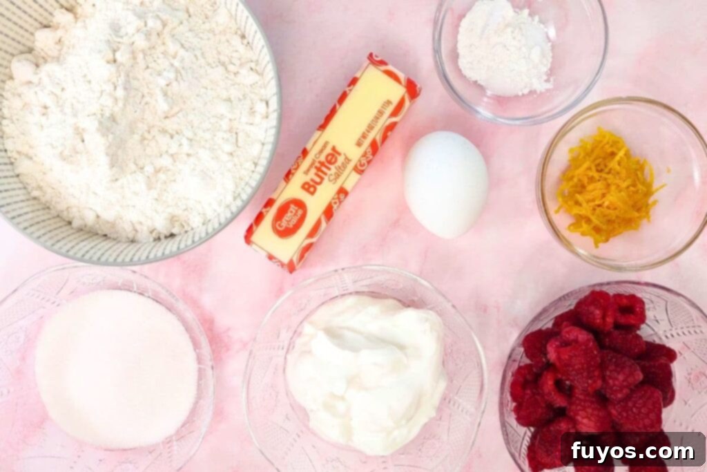 Various scone ingredients laid out on a wooden board, including flour, sugar, butter, eggs, raspberries, and oranges