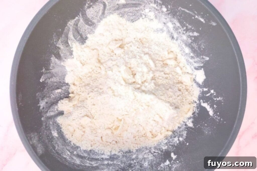 Mixing cold butter cubes into dry scone ingredients until a crumbly texture is achieved