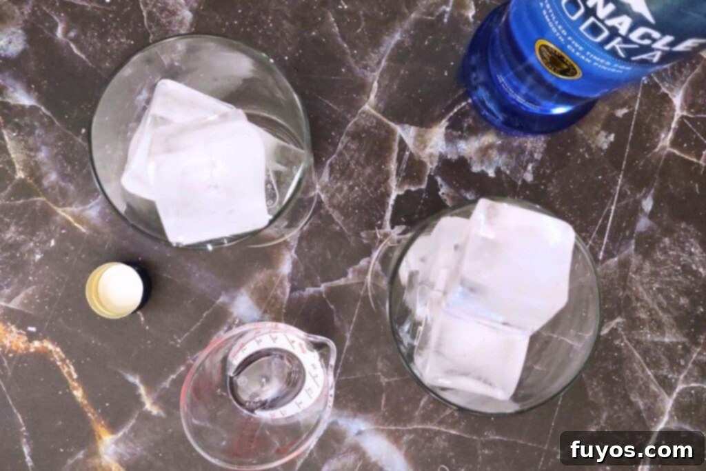 Vodka being poured over ice in a cocktail glass, creating the base of the drink.