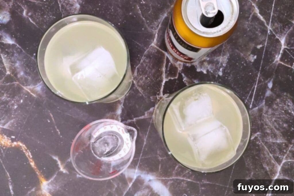 Ginger beer being poured into a glass already containing vodka and ice, filling it almost to the top.