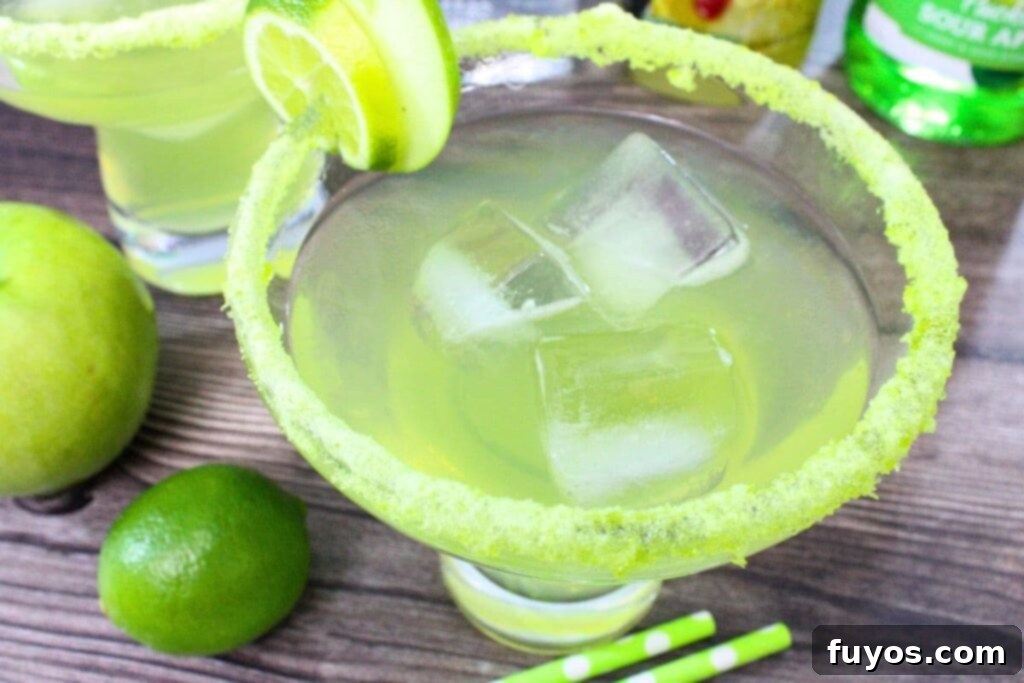 Sweet and Tart Green Apple Margarita Bliss 3 sour green apple margarita with crushed jolly rancher pieces on the rim