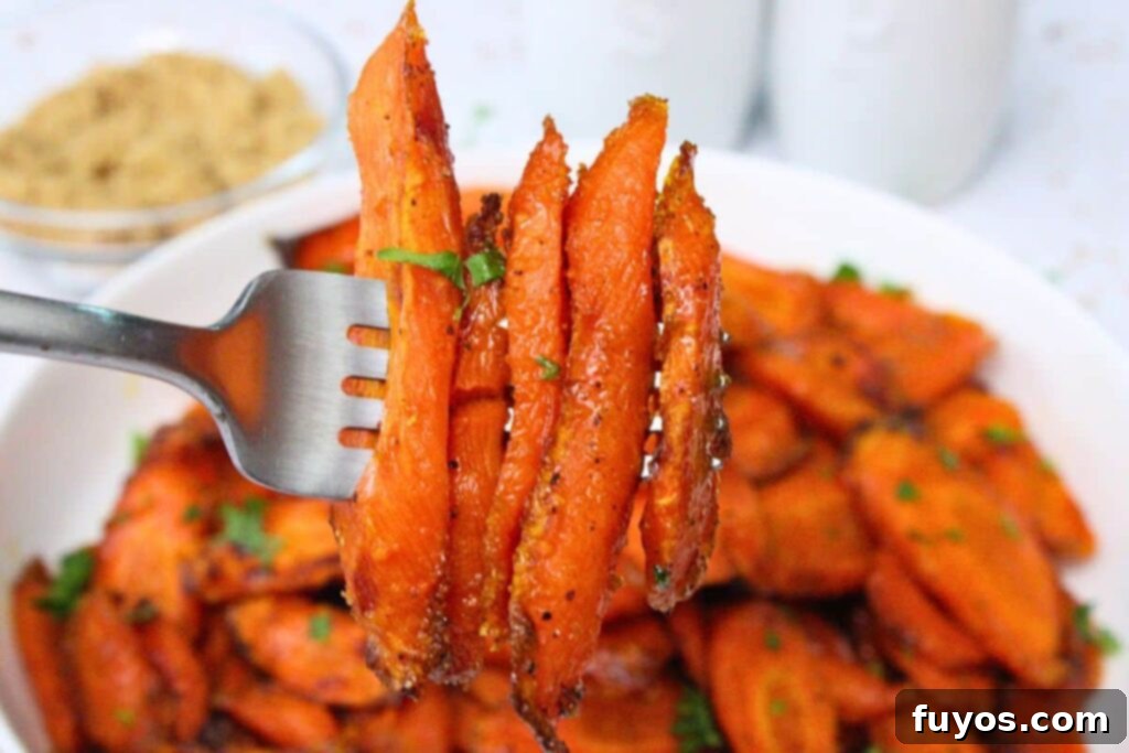 Delicious Air Fryer Brown Sugar Carrots Done in Ten Minutes 3 holding up a fork with slices of roasted air fryer brown sugar carrots over a bowl of more