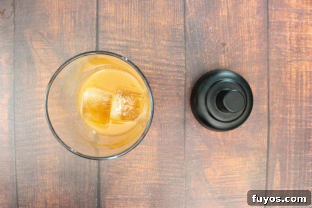Ingredients for spiced pear margarita – tequila, triple sec, pear syrup, lemon juice, and cinnamon – being poured into a cocktail shaker with ice.