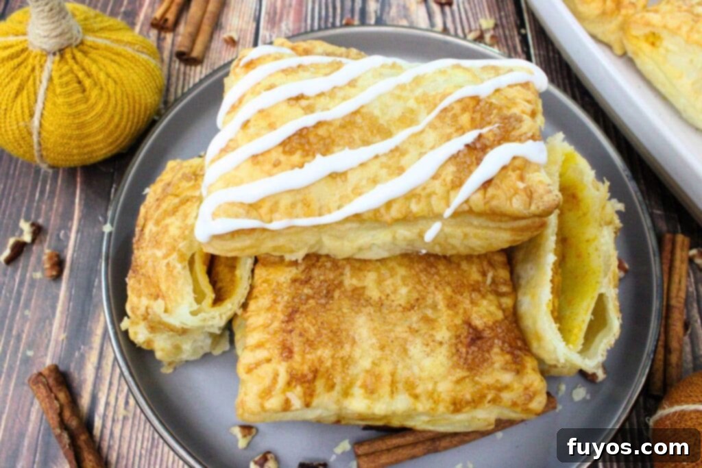 Autumn Air Fryer Pumpkin Puff Pastry Hand Pies 13 air fryer puff pastry pumpkin hand pies stacked on a plate with icing swirled on top