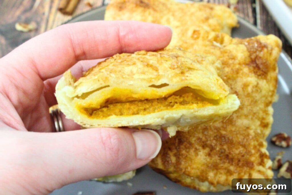 Autumn Air Fryer Pumpkin Puff Pastry Hand Pies 3 holding up a cut in half air fryer puff pastry hand pie with pumpkin filling