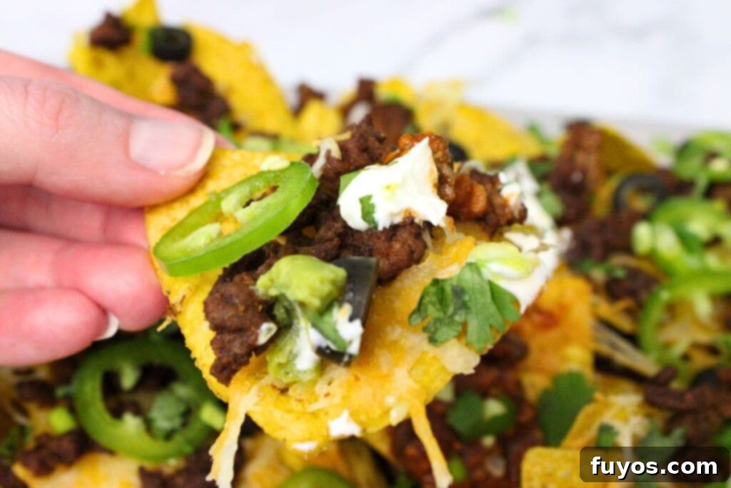 The Ultimate Air Fryer Nachos for Game Day 3 holding up an air fryer nacho chip with ground beef, jalapeno, sour cream, and black olives