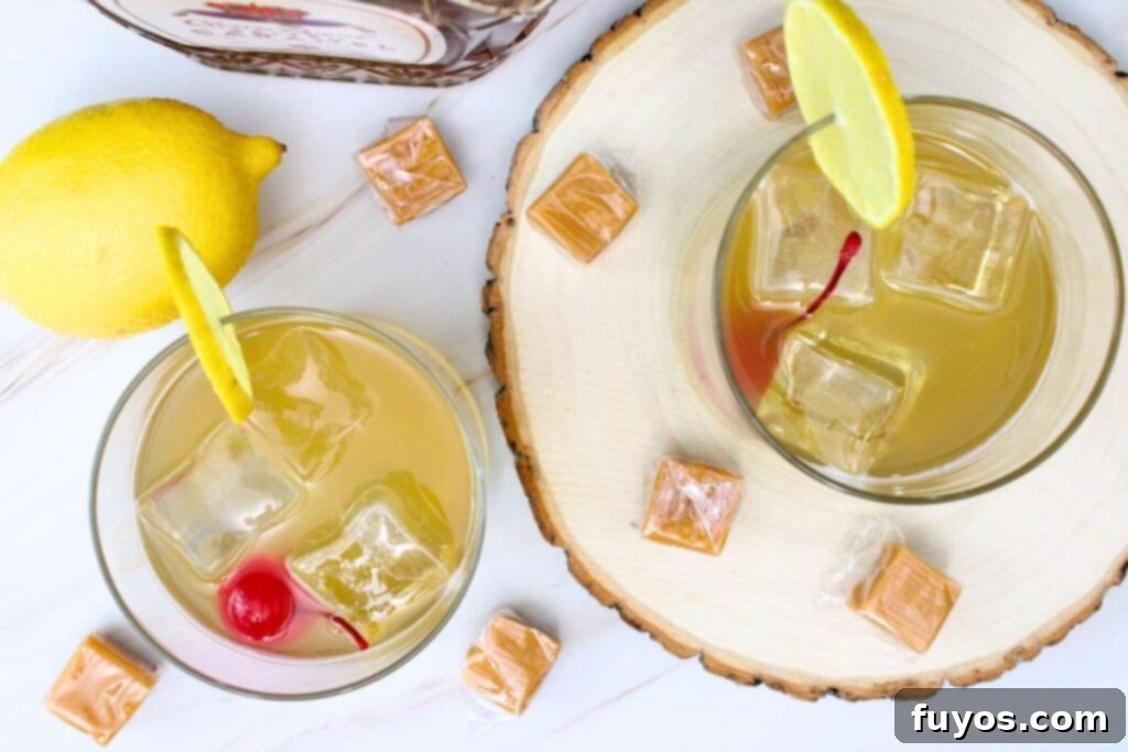 Overhead view of two perfectly garnished salted caramel whiskey sour cocktails, surrounded by caramel cubes