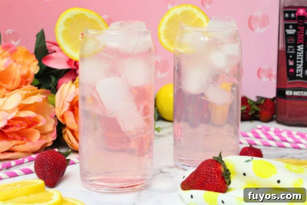 Pink Whitney and Sprite Recipe Easy 2 Ingredient Cocktail 9 Two perfectly prepared Pink Whitney and Sprite cocktails in tall glasses, garnished with lemon slices, set against a soft pink background.