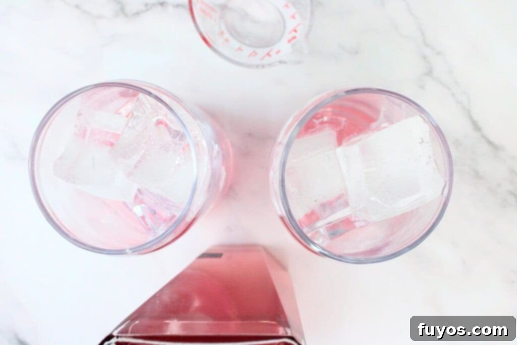 Pink Whitney and Sprite Recipe Easy 2 Ingredient Cocktail 6 Pink Whitney vodka being poured over ice cubes in a highball glass, creating a delicate pink swirl.
