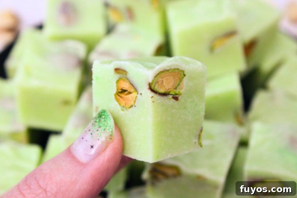 4 Ingredient Microwave Pistachio Fudge Delight 3 holding up a cube of creamy pistachio fudge with visible pistachio pieces