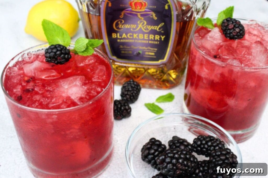 two glasses of crown royal blackberry smash cocktails with fresh fruit and the bottle in the background